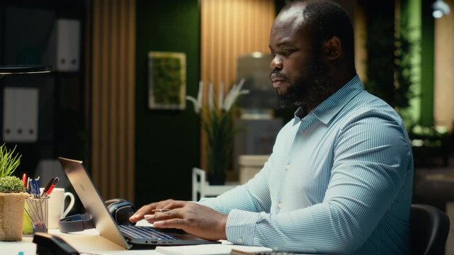 African american employee drafting updates and handwriting a summary late at night at the office. Data reports information with the monthly activity planner, business goals and agenda. Camera B.