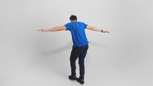 Back view of a Caucasian man walking on a narrow path holding hands by sides to keep balance and trying not to fall. Guy is stepping on an invisible rope being very careful filmed on white background.