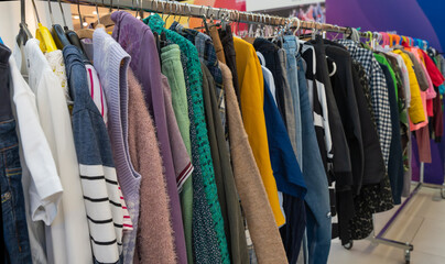 Obraz premium Various clothes hanging on racks at an eco swap event. Sweaters, shirts, and jeans in different colors and textures symbolize reuse, sustainability, and eco-friendly fashion choices.