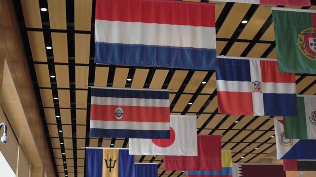 View of global country flags suspended from roof in modern hall Ceiling display of world flags including Costa Rica, Netherlands, Portugal, and others flags
