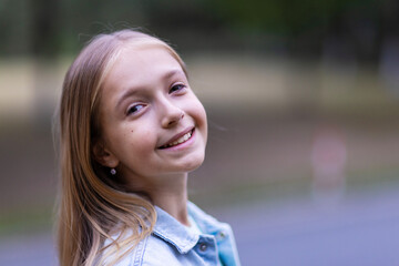 Smiling young girl with long blond hair standing outdoors in a park