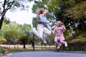 two sibling girls joyfully jumping while holding hands in a park