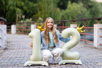 Smiling girl celebrating twelfth birthday with number balloons in outdoor park