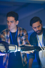 A diverse tech team collaborates on robotic arm prototypes. A Caucasian man assembles one, while his Indian colleagues, one wearing a bionic hand, analyze the process.