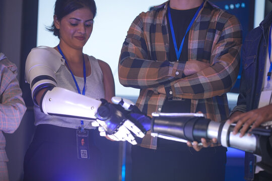 Engineers in an RD lab test a human-machine interface. A woman wearing an AI-powered prosthetic arm connects with another bionic prototype, testing its sensors and grip.
