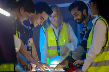 A logistics manager uses a radio to coordinate the supply chain on a night shift. The diverse team...