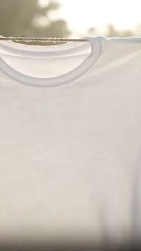 Close Up of Clean White T-Shirt Drying on Clothesline in Gentle Sunlight with Soft Background and Textured Fabric for Fashion Textile and Garment Industry Promotion and Laundry Product Ads