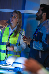 A diverse engineering team, a Caucasian woman in a safety vest and an Indian man, collaborates at...