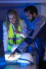 A diverse engineering team, a Caucasian woman in a safety vest and an Indian man, collaborates at...
