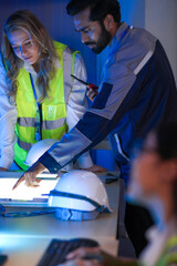 A diverse engineering team, a Caucasian woman in a safety vest and an Indian man, collaborates at...