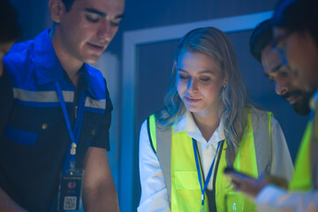 A large logistics team reviews supply chain blueprints. The diverse group, including an Indian...