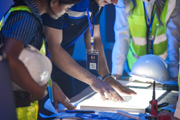 A happy engineering team reviews a CAD blueprint on a light table. They are in a smart factory control room, analyzing an AI-driven automation system plan at night.