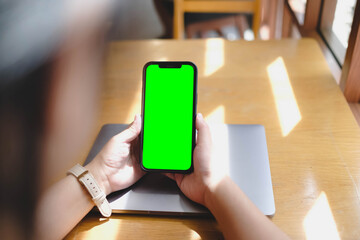 A person holding a smartphone with a green screen in a cafe. Ideal for chroma key compositing, video effects, and custom screen content placement.