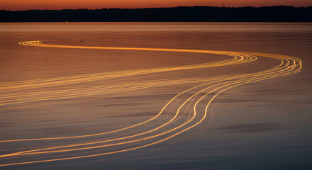 Long exposure light trails from boats on a calm lake at sunset.