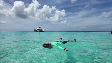 Child floating peacefully in turquoise sea. Relaxing vacation moment on water. Summer freedom and calm in ocean. Clear blue sea with yacht background. Serenity and joy during tropical travel.