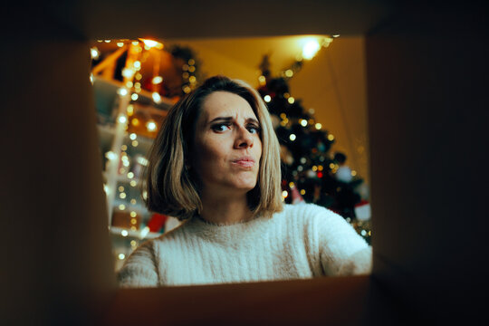 Puzzled Woman Looking Inside a Gift Box on Christmas. Frowning girlfriend being curious what she received for Christmas