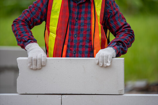 A construction worker in a plaid shirt and safety gear carefully places a concrete block at a building site, showcasing dedication to quality and safety in the construction industr