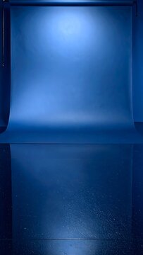 Empty blue photography studio background with a seamless paper sweep spotlight and reflection.