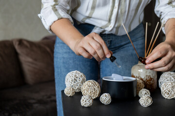 Unrecognizable woman adding essential oil to Close up of home perfume scent air humidifier with light. Aromatherapy holistic health practices concept. Stress relief activities preparing for meditation
