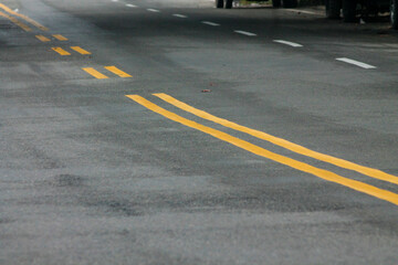 Yellow Lines on a Winding Road. Abstract turning road background with tires track and yellow striped road marking on dark asphalt.	
