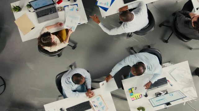 Top down view zoom in of employees engaged in business intel and analytics using data diagrams in office, staff reviews projections and reports to improve overall company strategy. Camera A.