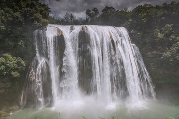 Close up on the Huangguoshu Waterfall in Guizhou Province, China, people walking under the waterfall create a scale