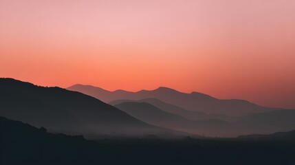 Fototapeta premium Layered mountain silhouettes glow against a vibrant orange and pink twilight sky
