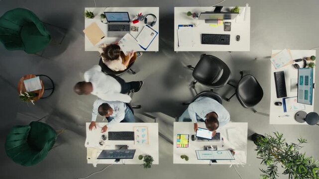 Time lapse top down view of diverse colleagues working in office, focusing on project planning, performance metrics and report sharing. Business people review data for forecasting. Camera A.