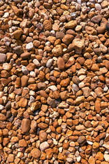 A collection of small brown and tan stones covers the ground with rough uneven textures and natural variation in shape and color forming an earthy and organic rocky surface