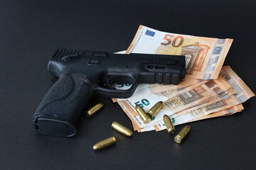 Close-up of a black handgun with euro banknotes and bullets on a dark background, symbolizing crime, corruption or illegal finance concepts.