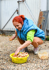 A 50-year-old Russian woman in a village prepares marinated chicken wings and thighs for grilling outdoors, smiling while skewering the meat on a stick.
