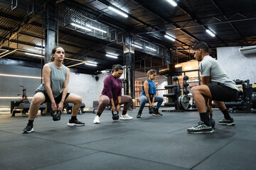 Group of latin american people performing kettlebell squats during a fitness training session at an modern gym