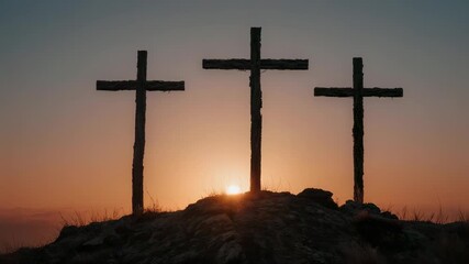 Three crosses silhouetted against a sunset sky on a grassy hill representing calvary or easter