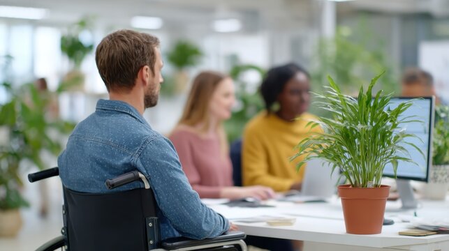 In an Office Setting, a Man in a Wheelchair Engages with Colleagues Amidst Lush Greenery and Modern Workstations