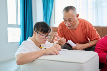 Fototapeta premium A man with Down syndrome is sitting at home doing his math homework with his teacher