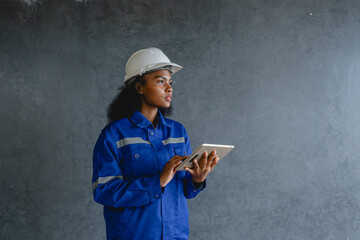 Portrait engineer woman wearing safety helmet and uniform holding  digital tablet standing gray...