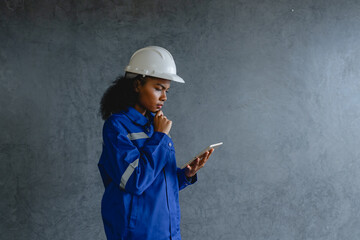 Portrait engineer woman wearing safety helmet and uniform holding  digital tablet standing gray background appears focused and professional representing modern technology construction.