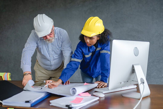 engineer wearing uniform sitting in front of computer, reviewing blueprints and documents achievement project in construction work concept.