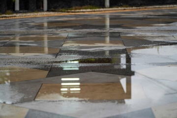 Wet pavement with reflections of a building after rain.