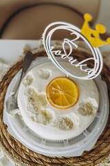 Elegant minimalist birthday cake with smooth white icing, decorated with a dried orange slice and a golden crown topper reads “2 years”, celebrating a second birthday
