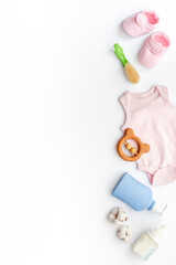 Flat lay of baby accessories - bodysuit and booties with wooden teether toys and bottle of milk on white background, top view