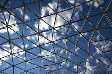 Modern glass dome's triangular framework against a vibrant blue sky with fluffy clouds