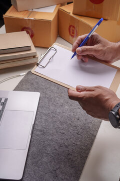 Small Business Owner Writing on Clipboard with Shipping Boxes