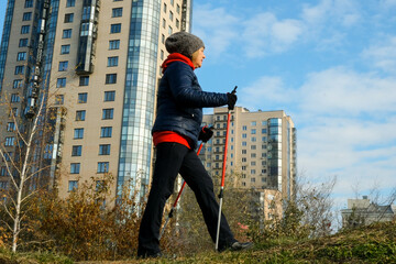 A full-length portrait of a Caucasian woman wearing a jacket and hat with Nordic walking poles...
