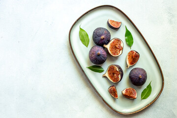 Purple ripe figs and slices with leaves on a plate top view on a stone background