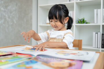 Naklejka premium Happy Asian children relax read book at home. daughter and reading a story. learn development, childcare, laughing, education, storytelling, practice, imagine, reduce addiction mobile phone