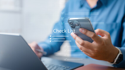 Businessman using smartphone and laptop with digital checklist interface, representing task management, project tracking, and productivity planning in modern office work.