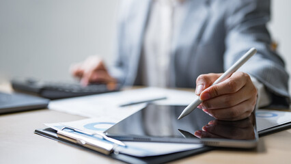 Businessperson using a digital tablet and stylus with financial reports, representing data analysis, audit review, and strategic project management in modern office work.