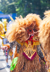 Vibrant Indonesian folk performance art. A participant from Sleman wears an elaborate mask and costume representing a mythical creature during Bandung's Asia Africa Carnival.