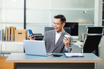 Fototapeta premium Asian man using laptop and tablet while sitting at her working place. Concentrated at work.